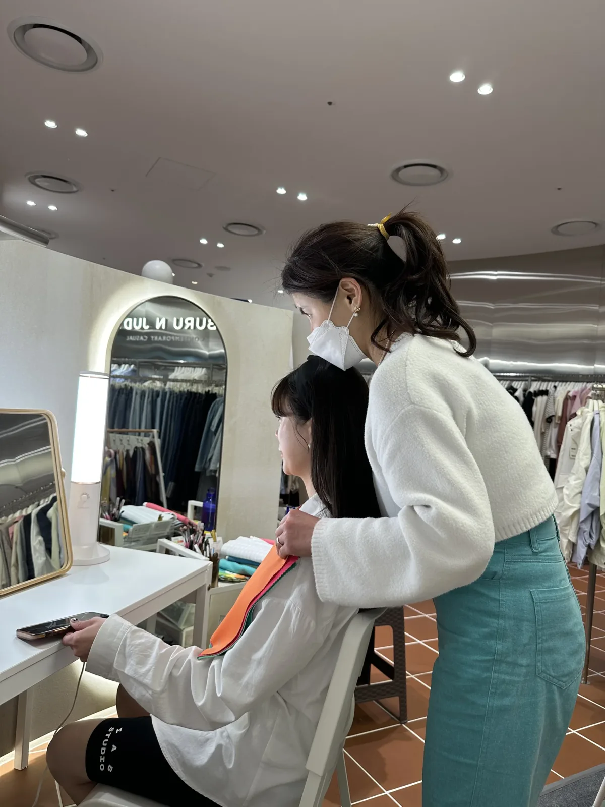 매장 거울 앞에서 고객 어깨에 주황색 컬러 원단을 올려 톤을 비교하는 진단 모습